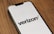 A smartphone lies on a wooden surface displaying the Verizon logo on its screen. The phone is positioned at an angle, showcasing the logo prominently against a white background.