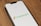 A smartphone is placed on a wooden surface displaying the Instacart logo on its screen. The logo consists of the word 'instacart' in green, accompanied by a carrot icon to the left.