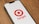 A smartphone displays the Target logo, featuring a red bullseye and the word 'target' in red, on its screen. The phone is placed on a wooden surface.