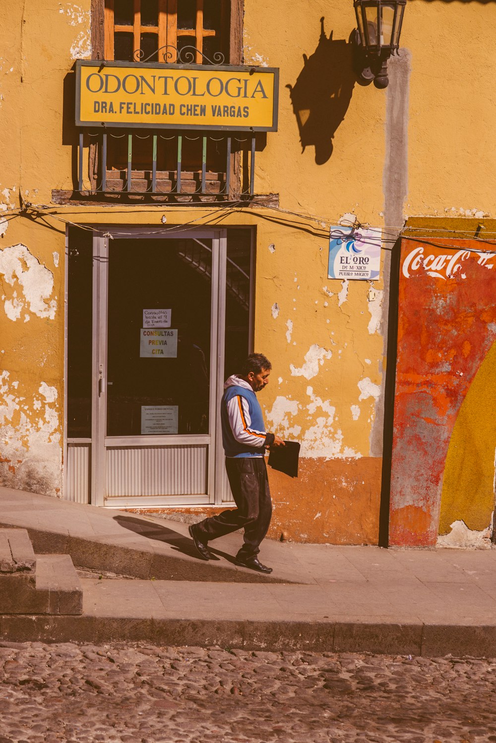 a man walking down a street past a yellow building