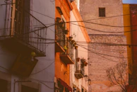 Golden hour light illuminating the intricate iron balconies and rustic doors of colonial homes.