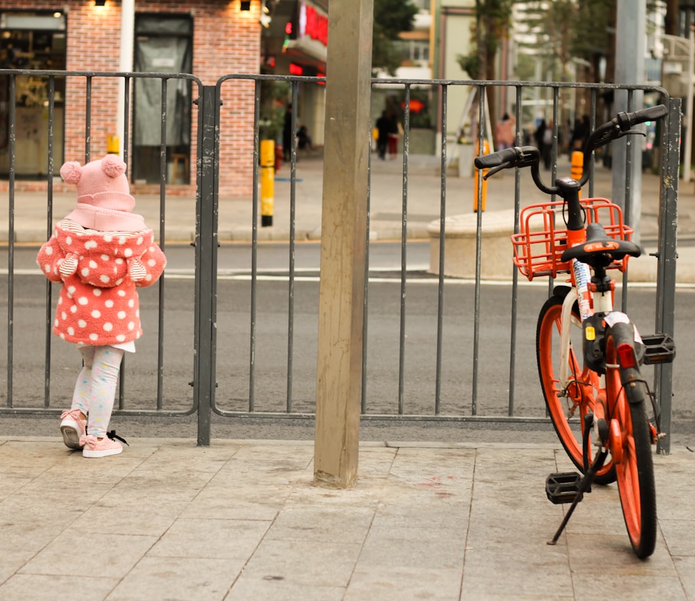 a little girl standing next to a red bike