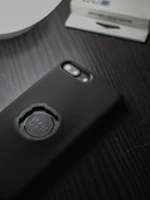 A smartphone with a black case featuring a circular mount labeled 'Quad Lock' is placed on a dark wooden surface. Part of a white dish and a packaging box are visible in the background.