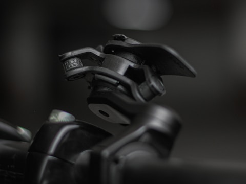 A close-up shot of a mechanical device featuring a hinge and clamp system, primarily made of metallic components. The device appears robust and industrial, positioned against a blurred background that highlights its detailed construction and texture.