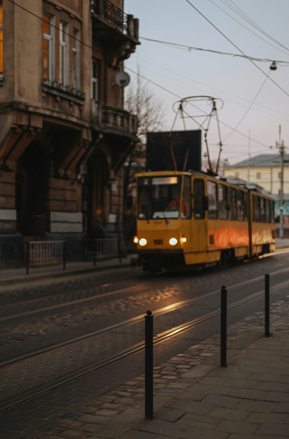 a yellow train traveling down a street next to a tall building