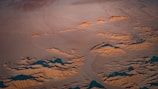 An aerial view of a desert landscape with red dunes under a bright blue sky.