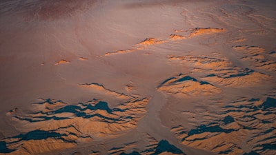 An aerial view of a desert landscape with red dunes under a bright blue sky.