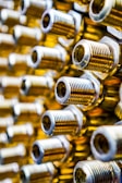 A close-up view of several threaded cylindrical metal objects, possibly bolts or connectors, arranged in a pattern. The metal surfaces have a shiny, polished appearance with golden and silver tones. The image has a shallow depth of field, creating a blurred effect in the background.