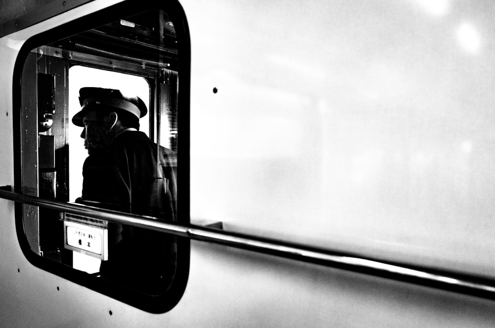 a black and white photo of a man looking out a train window