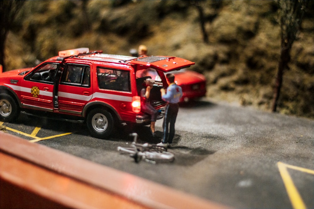 Una escena en miniatura de un coche rojo con un hombre de pie junto a él