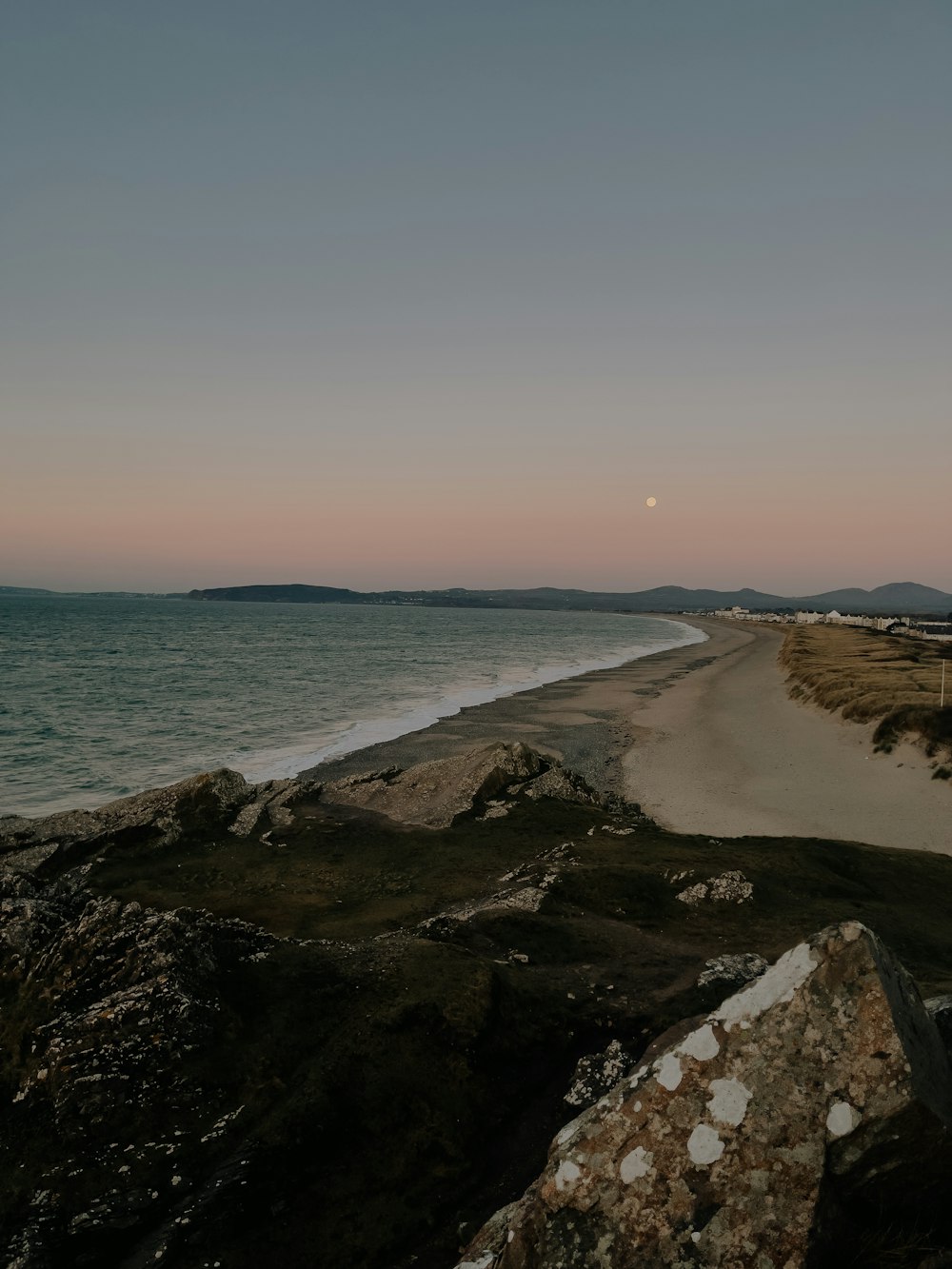 uma vista de uma praia com uma lua cheia à distância