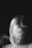 A blurred and abstract black and white image featuring a ghostly figure with indistinct facial features, creating a sense of movement and mystery. The darkness surrounding the subject enhances the ethereal and haunting quality.