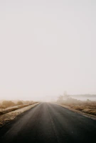 A cinematic shot of an empty coastal road disappearing into thick fog under a moody sky.