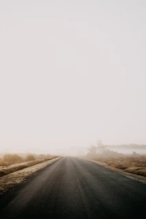 A cinematic shot of an empty coastal road disappearing into thick fog under a moody sky.