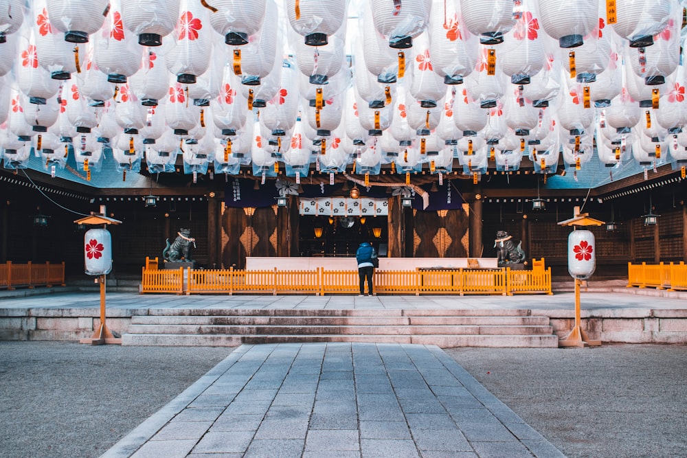 a person standing in front of a building with lanterns hanging from the ceiling