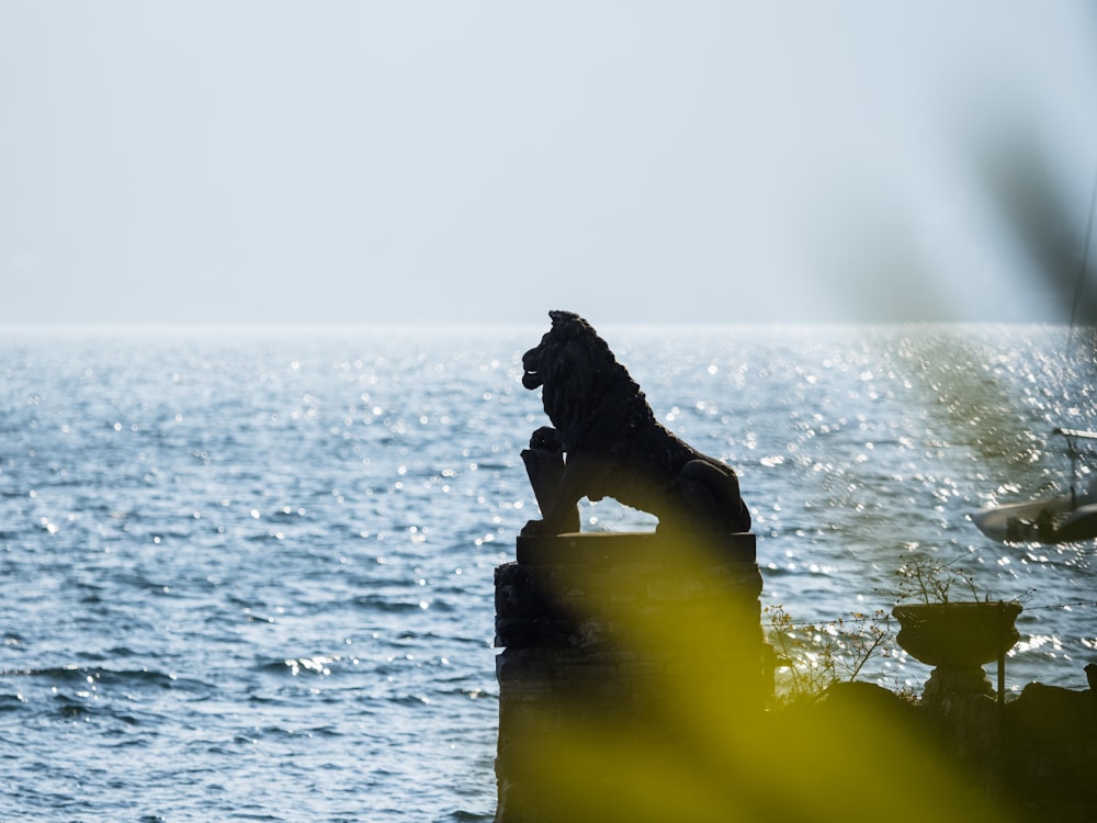 a statue of a lion sitting on top of a rock next to the ocean