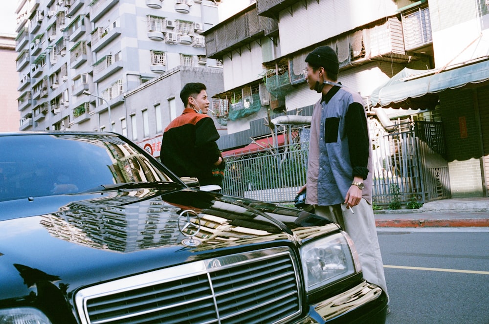 a couple of men standing next to a parked car