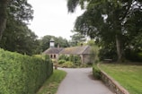 Exterior view of a quaint cottage surrounded by tall trees and a stone path.