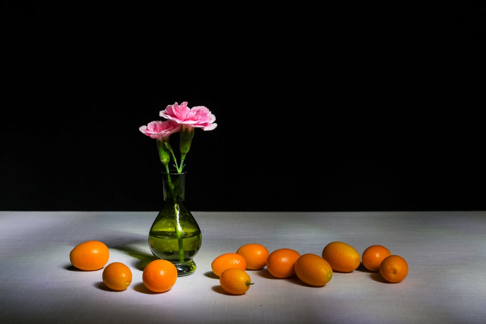 a vase with flowers and oranges on a table