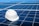 A white hard hat rests on a large array of blue solar panels under a clear sky. The panels are aligned in an orderly fashion, reflecting sunlight and emphasizing a clean energy theme.