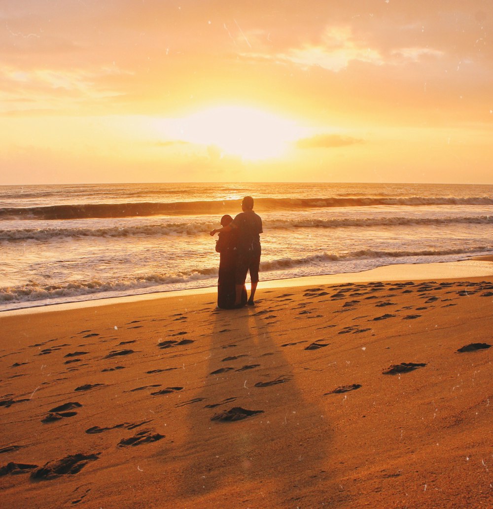 a couple of people standing on top of a sandy beach