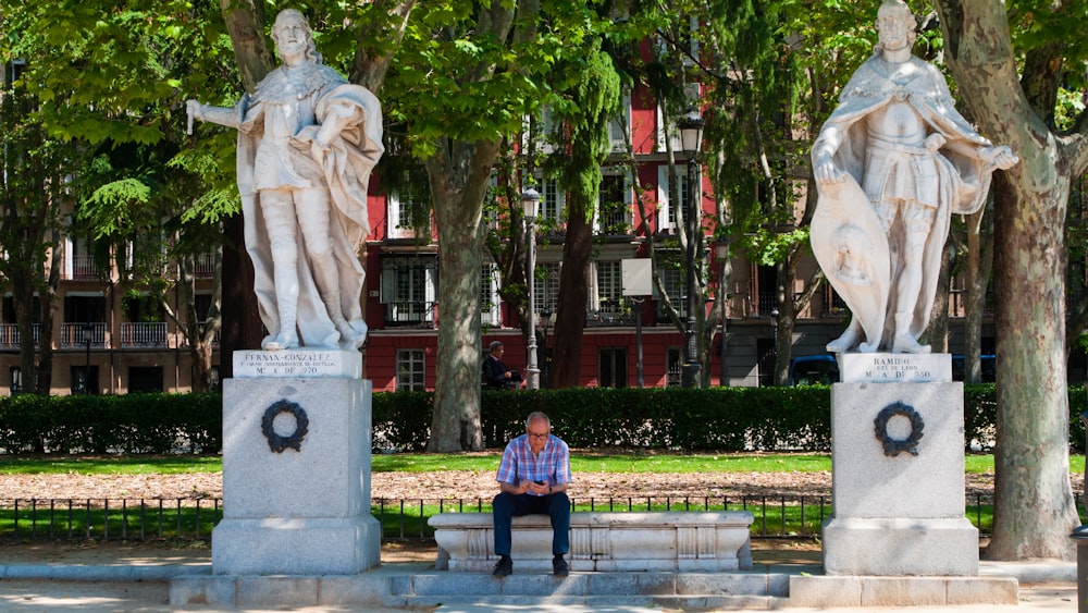 a man sitting on a bench next to two statues