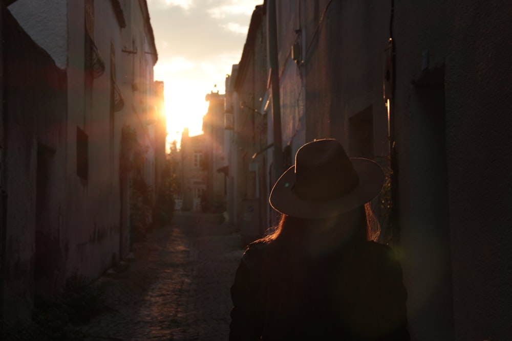 a woman in a hat is walking down an alley way