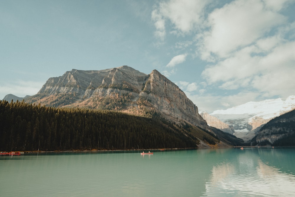 a lake surrounded by mountains and trees under a cloudy sky