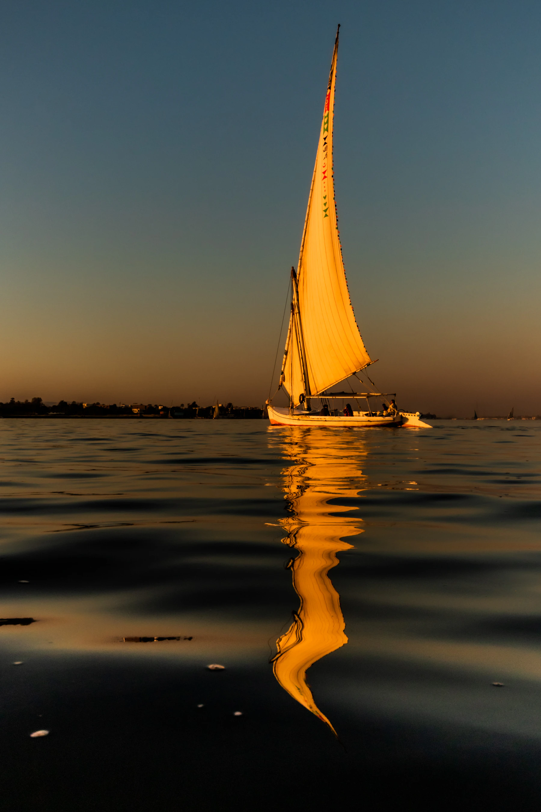 A felucca sails on the Nile at Luxor with the west bank beyond.
