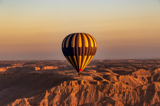 A colorful hot air balloon floating over a scenic landscape at sunrise.