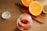A jar filled with colorful gummy vitamins is placed on a wooden table. The jar is open, with the cap lying beside it. In the background, there is a wooden cutting board with halved oranges, a lemon, and a lime, adding a vibrant touch to the scene.