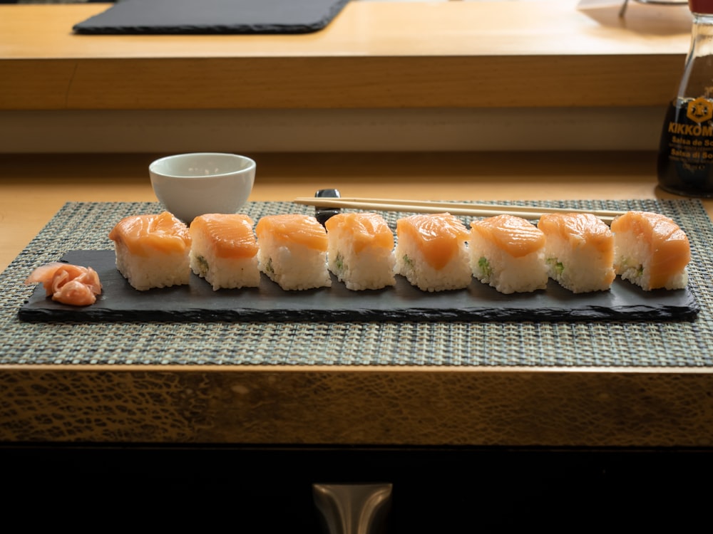a plate of sushi with chopsticks and a bowl of sauce