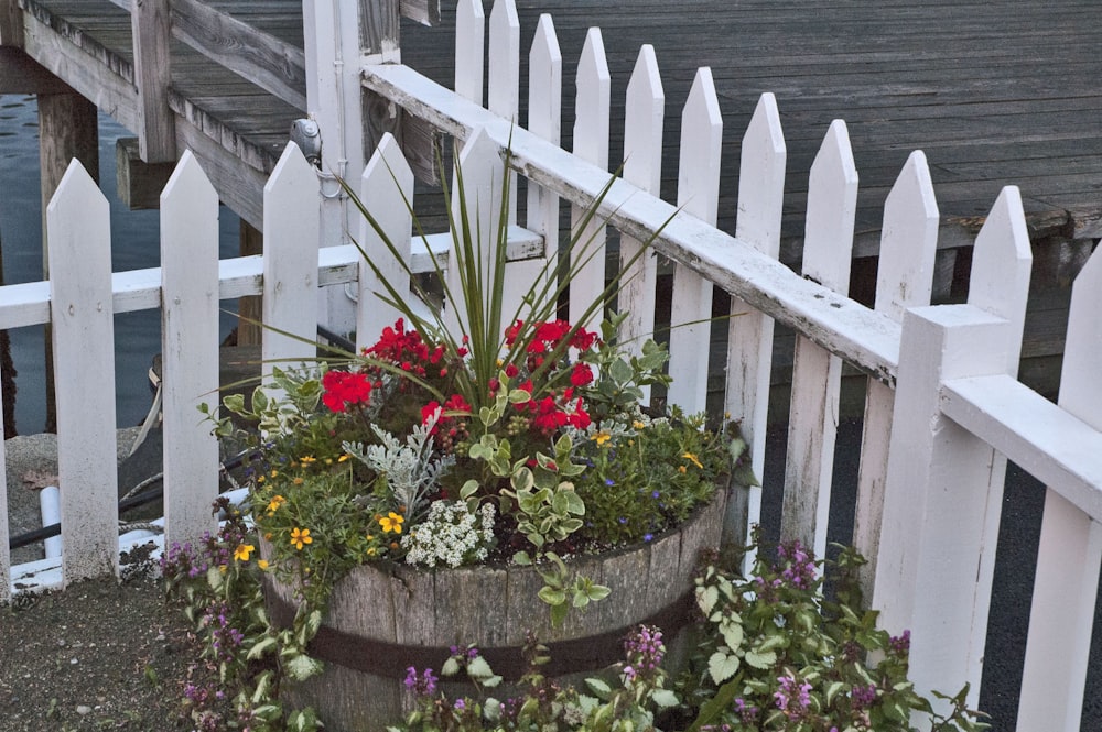 a wooden bucket filled with flowers next to a white picket fence