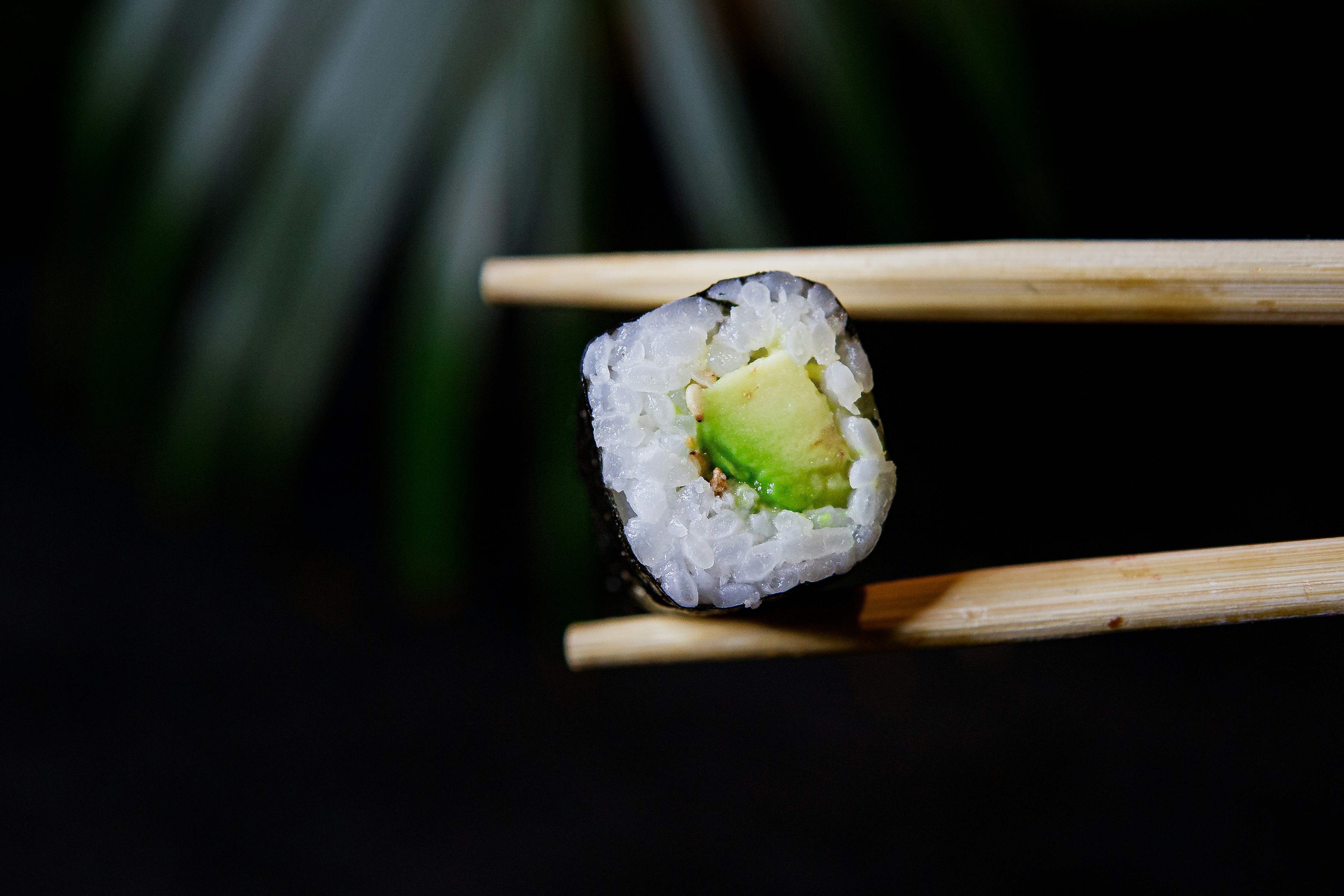 a piece of sushi on chopsticks with a piece of avocado