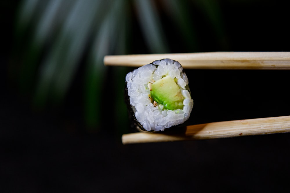 a piece of sushi on chopsticks with a piece of avocado