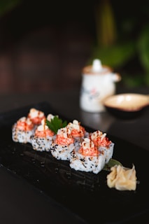 Elegant arranged sushi rolls with a drizzle of spicy mayo on a dark ceramic plate.