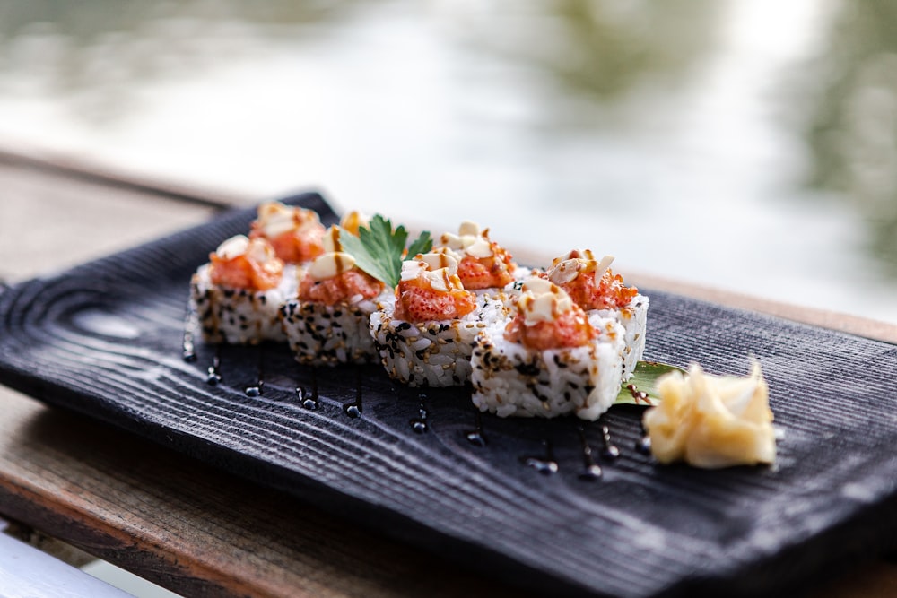 a black plate topped with sushi on top of a wooden table