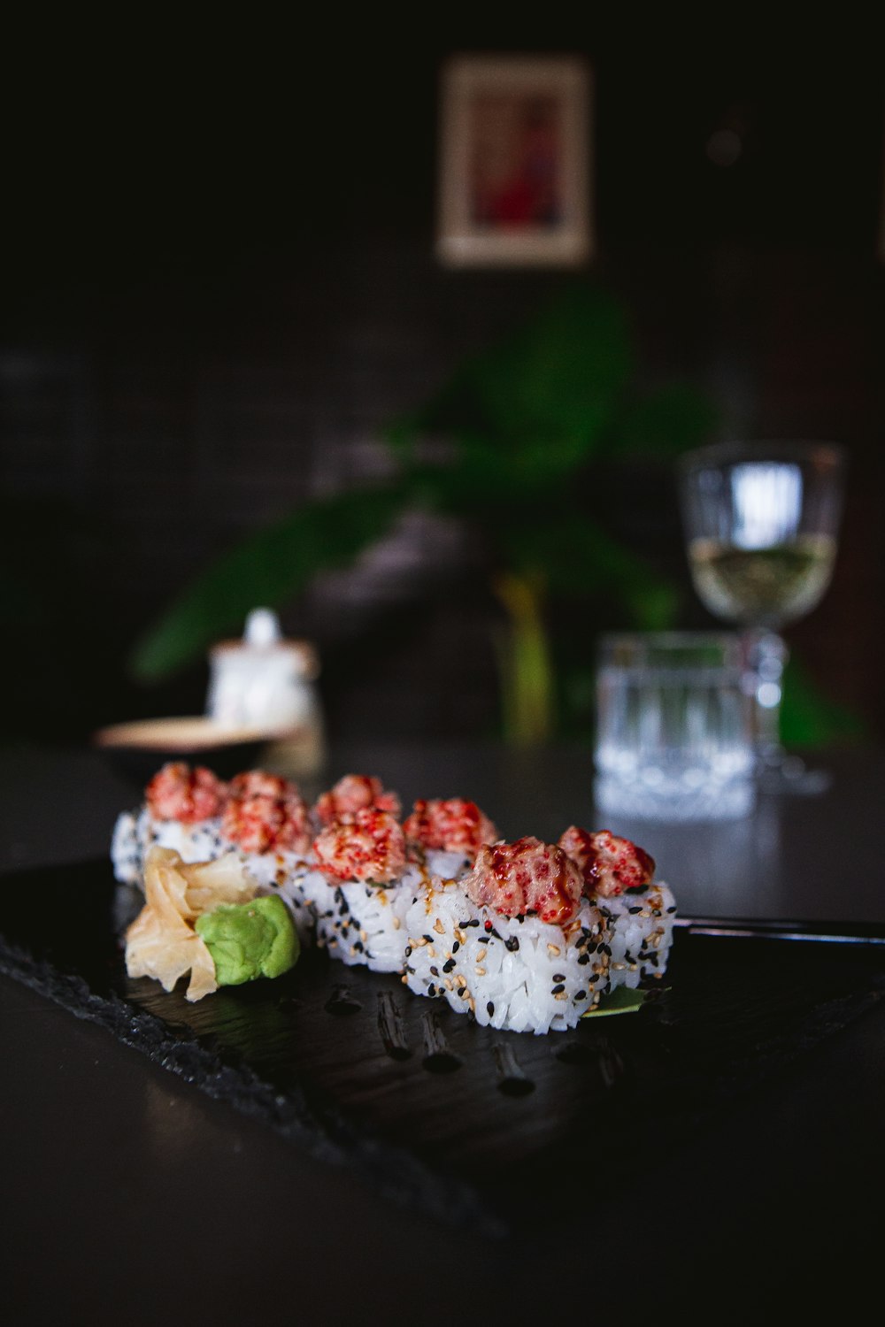 a black plate topped with sushi next to a glass of wine