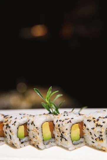 A close-up of a vibrant sushi roll topped with fresh avocado and drizzled with spicy mayo.