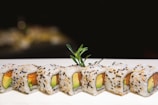Close-up of a colorful sushi roll with avocado and salmon on a black plate.