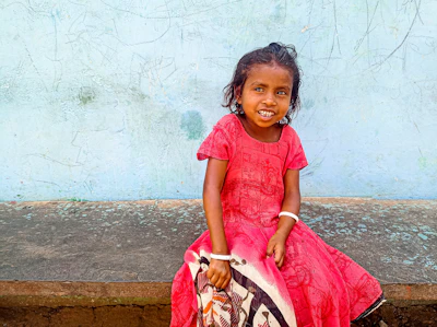 A joyful young girl dressed in a pastel pink lehenga choli, smiling in a softly lit festive setting.