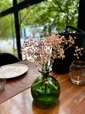 A soft green ceramic vase sitting on a wooden table with fresh wildflowers.
