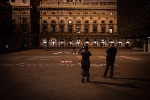 A black and white photo of a community gathering in an open plaza at dusk