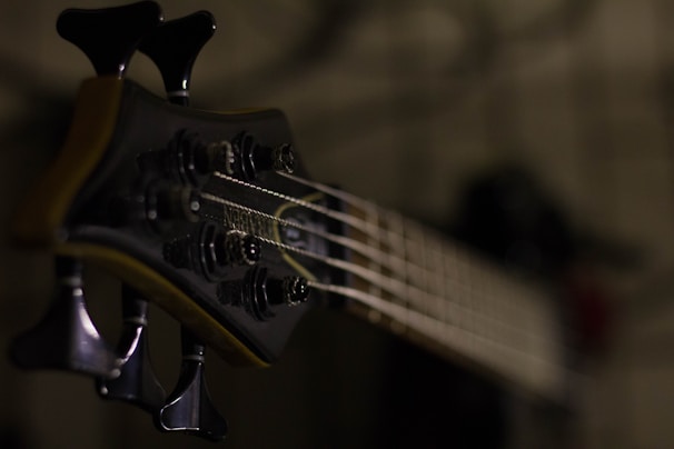 A close-up of a bass guitar headstock, with strings running down the neck. The focus is on the tuning pegs, dark in color, enhancing the instrument's elegant design.