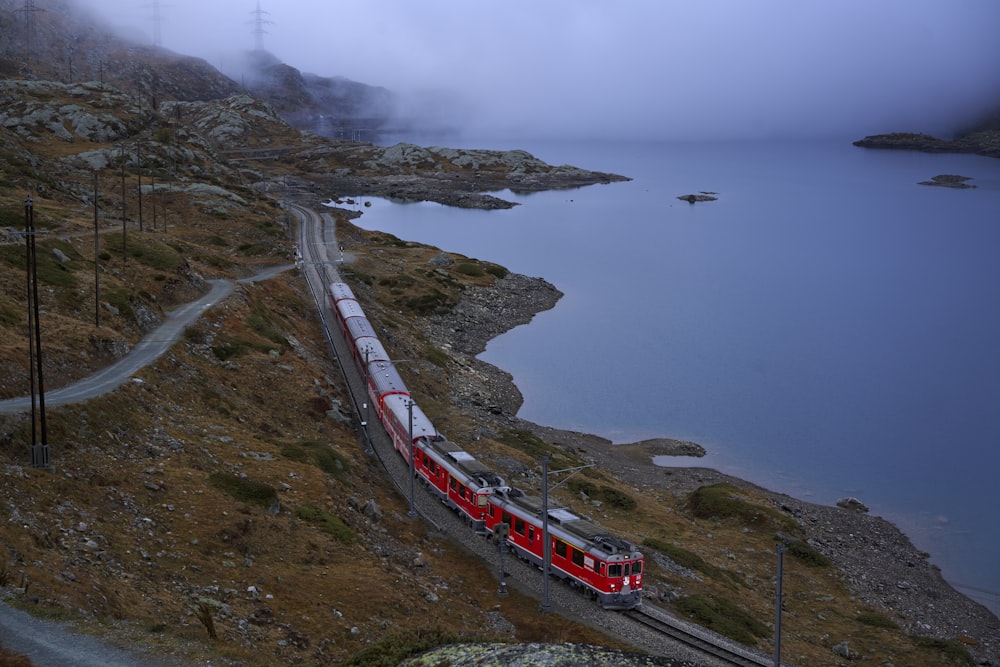 a red and white train traveling down train tracks next to a body of water