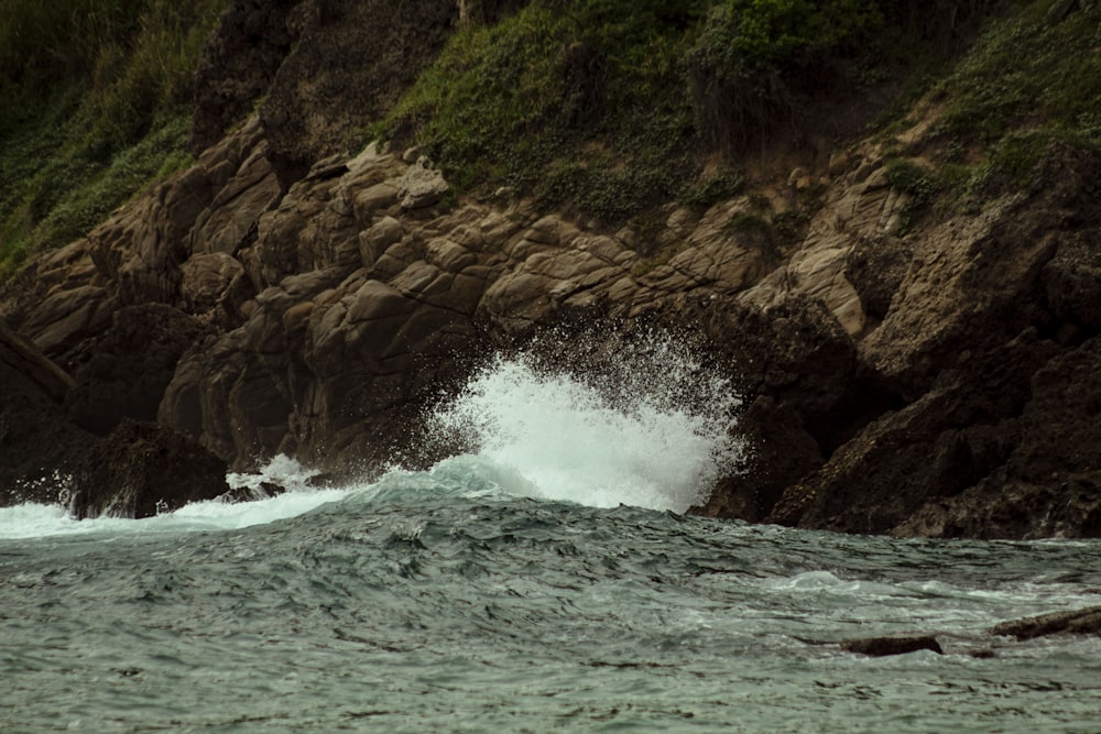 a wave crashing into a rocky shore next to a cliff