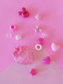 A collection of pastel-colored polymer clay charms arranged on a glittery pink background.