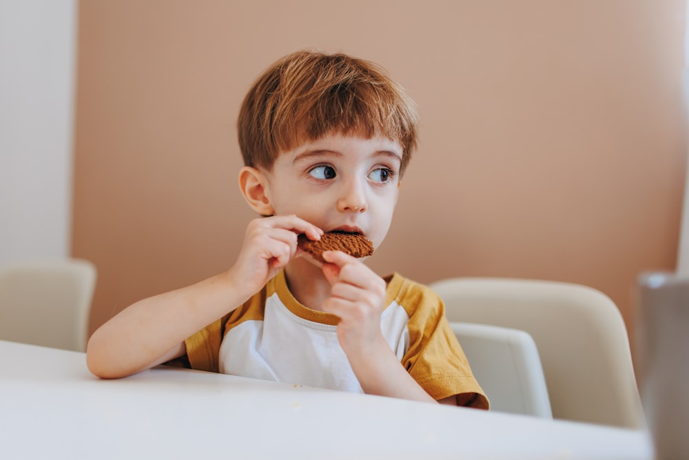 um menino sentado em uma mesa comendo um donut de chocolate
