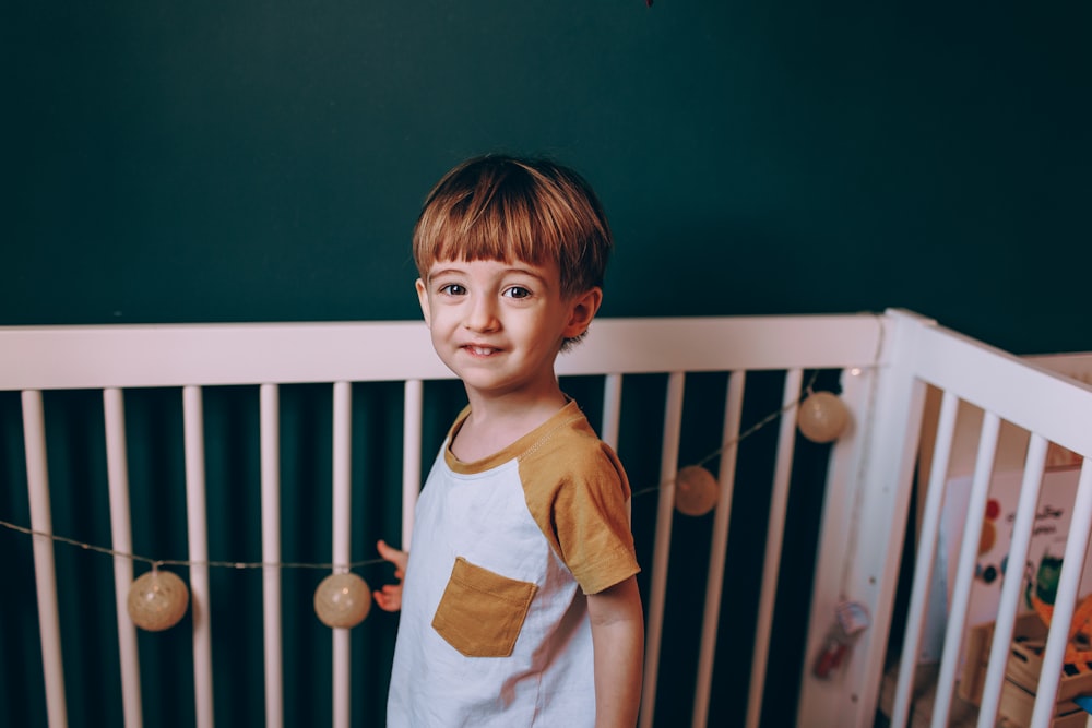 a young boy standing next to a crib