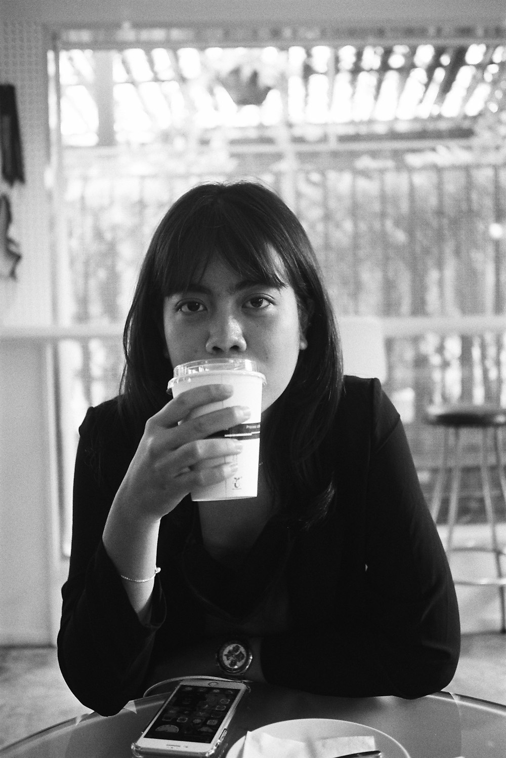 a woman sitting at a table drinking from a cup